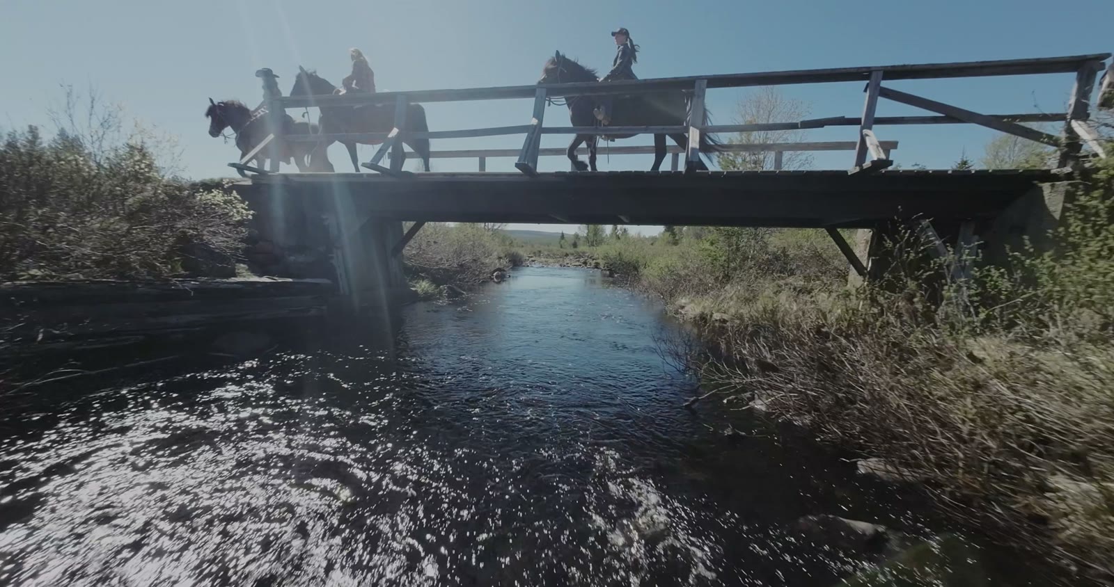 Riders crossing a wooden bridge, filmed from the water